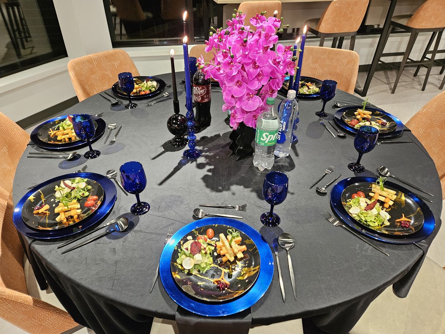 Round banquet table with dark linen, blue glasses and pink orchids